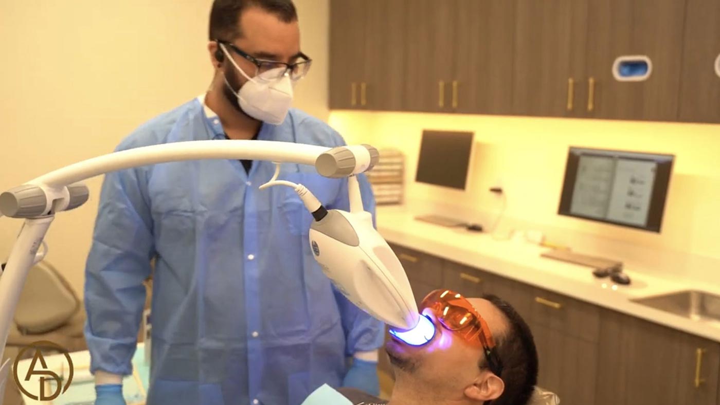 A dentist is using a teeth whitening laser on a patient.