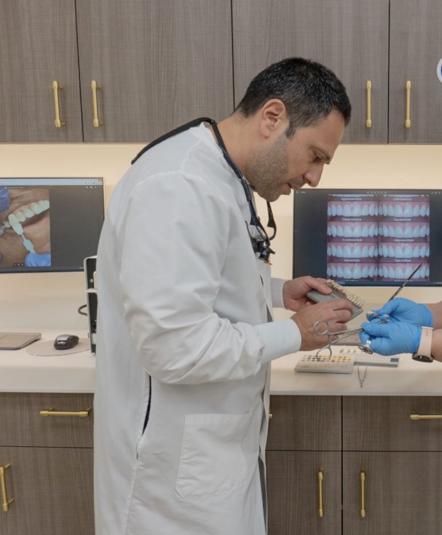 A dentist is holding a shade guide up to a patient's teeth to determine the correct shade for a veneer.