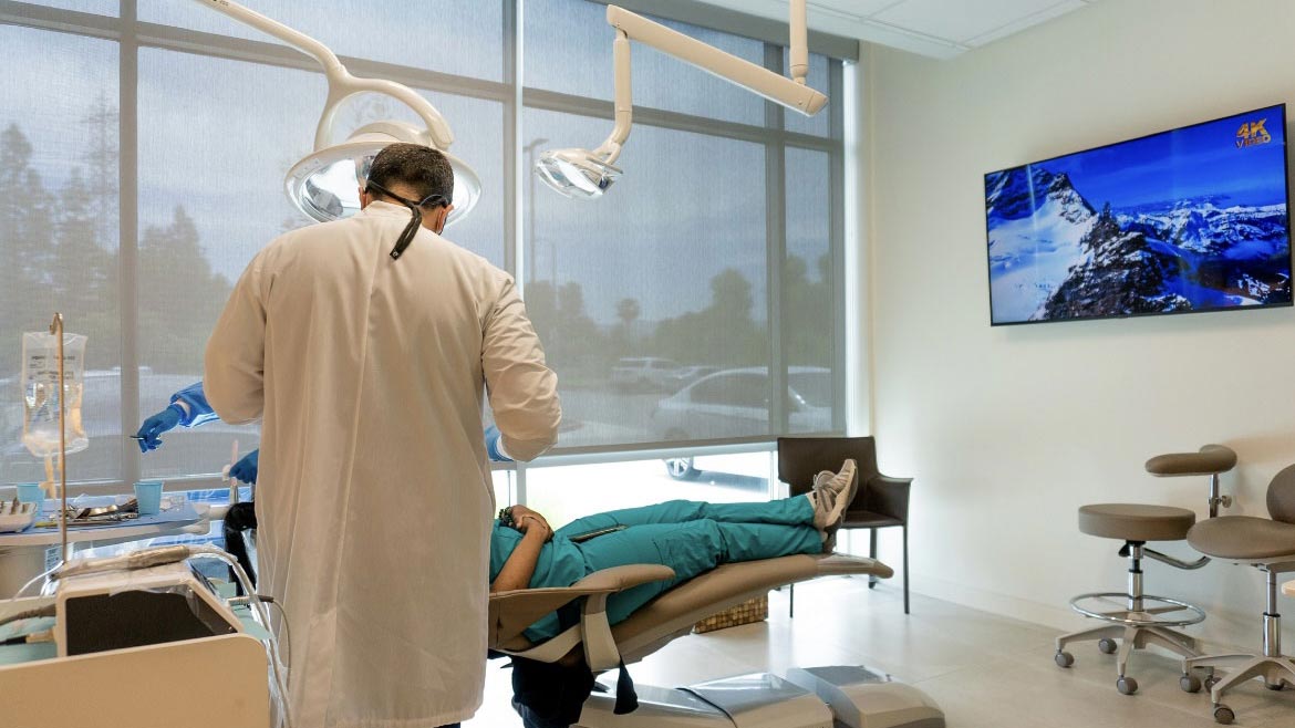 A dentist is working on a patient's teeth while the patient is reclined in a dental chair.