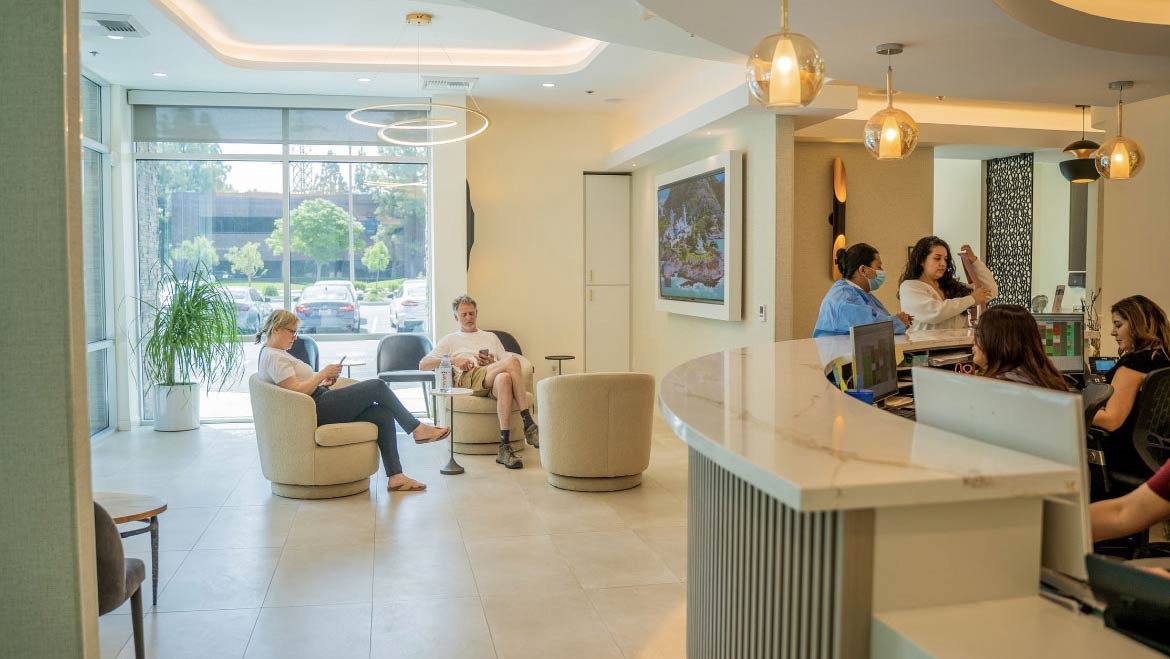 A modern dental office with a curved reception desk, comfortable seating, and large windows.