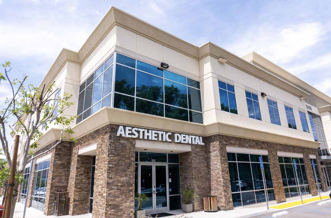 The image shows a modern dental office with a stone and glass exterior. The name of the business is 