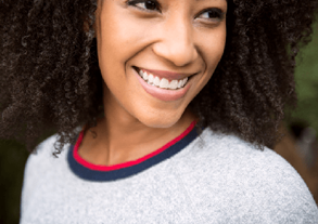 The image shows a young woman with curly hair smiling.